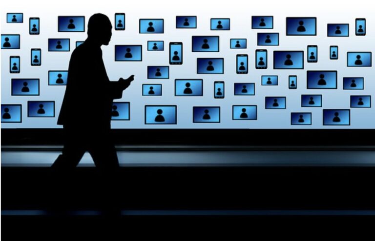 silhouette of a man walking in front of monitors
